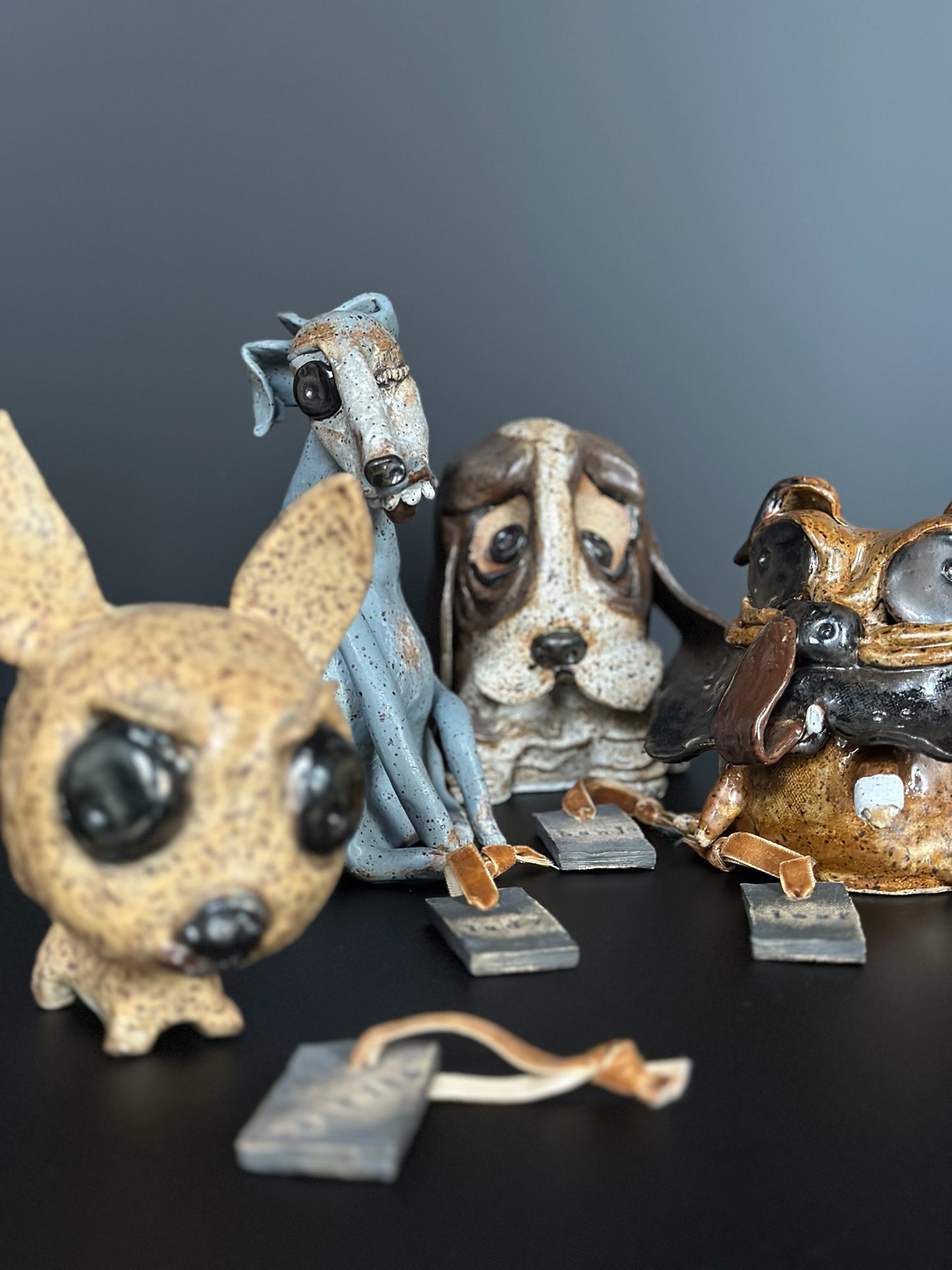 Four dog figurines in different colors on a dark surface with a gray background