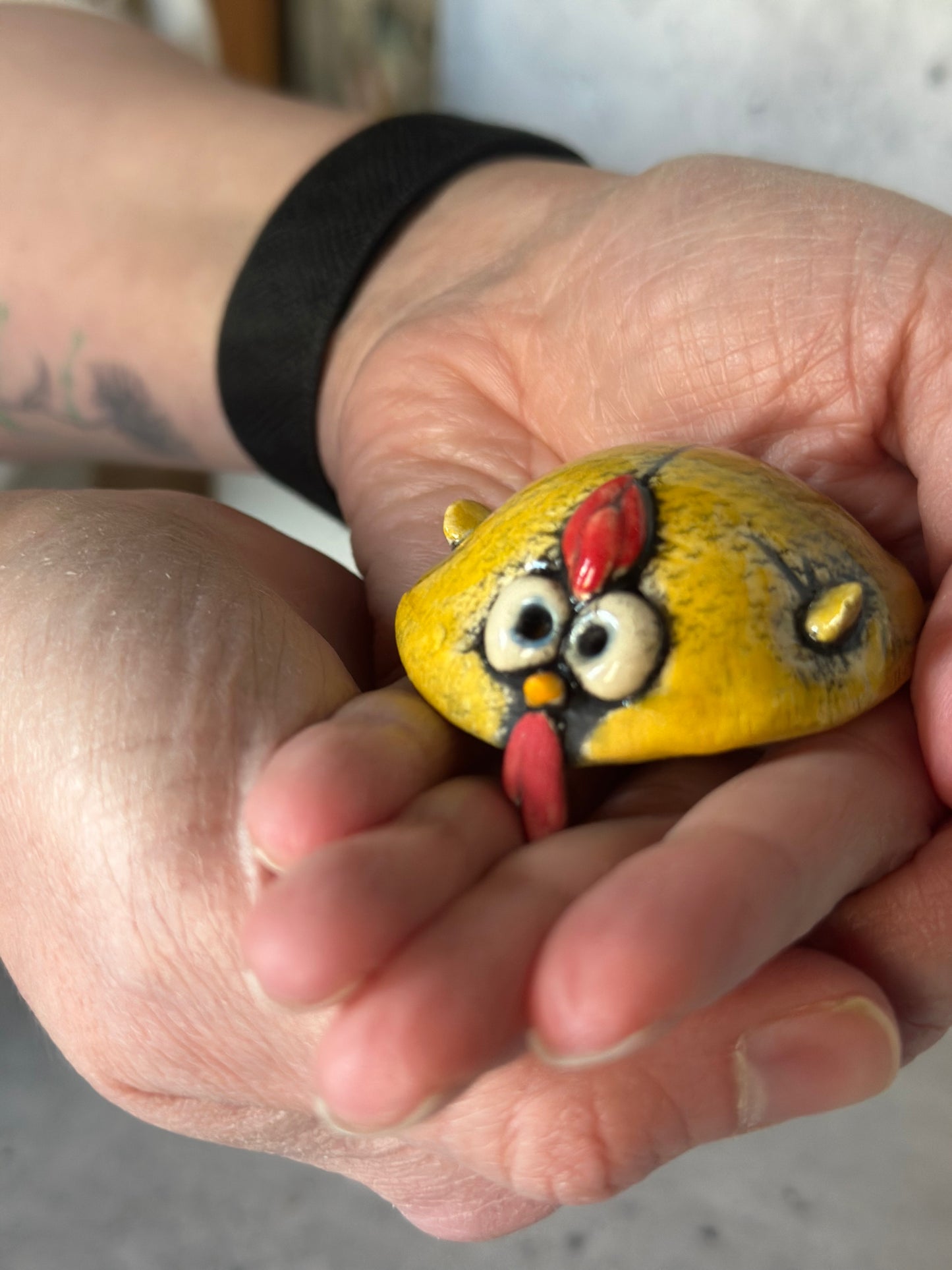 Hand holding a painted rock with a rooster design