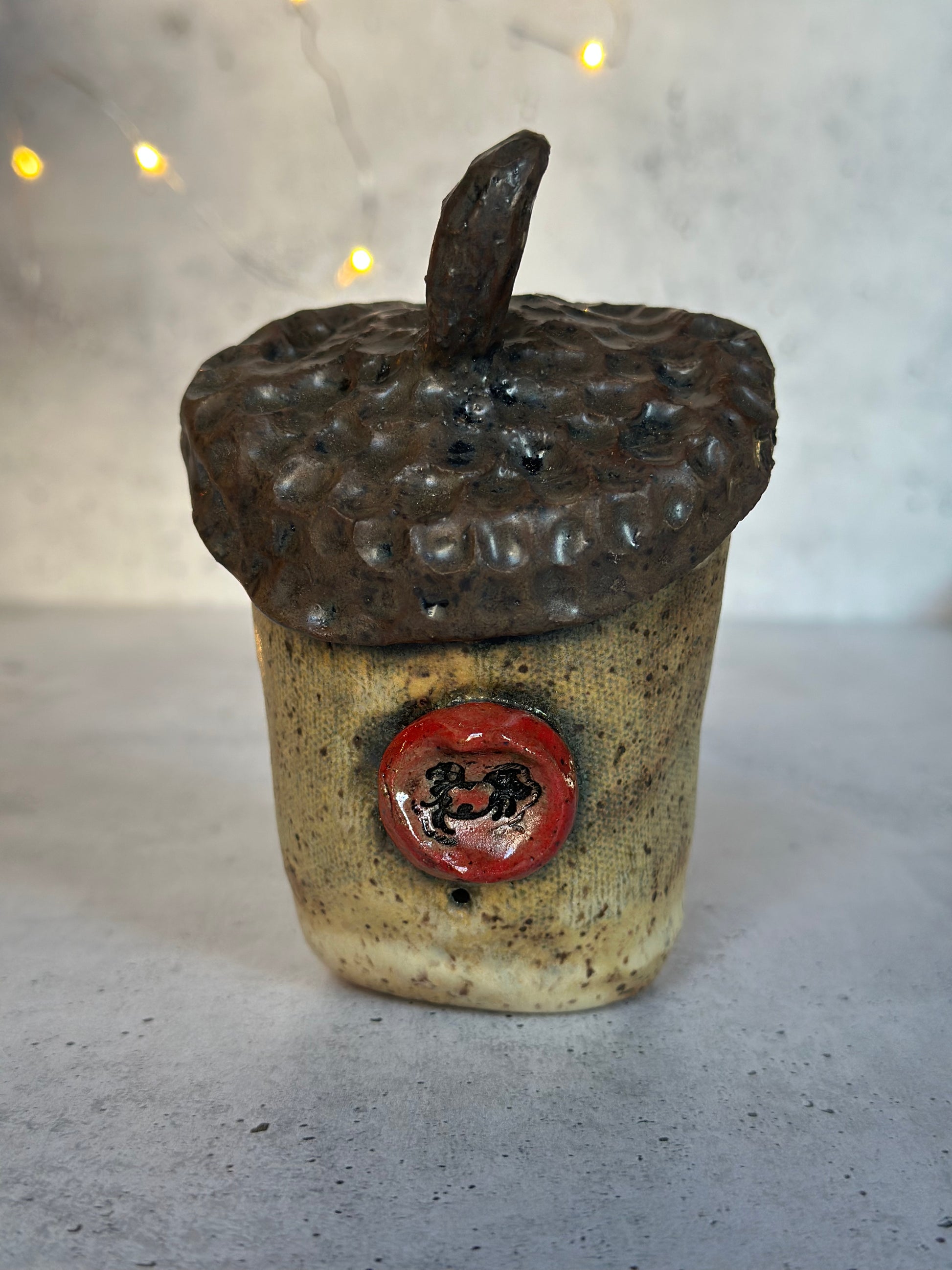 Ceramic acorn-shaped container with a red emblem on a gray surface