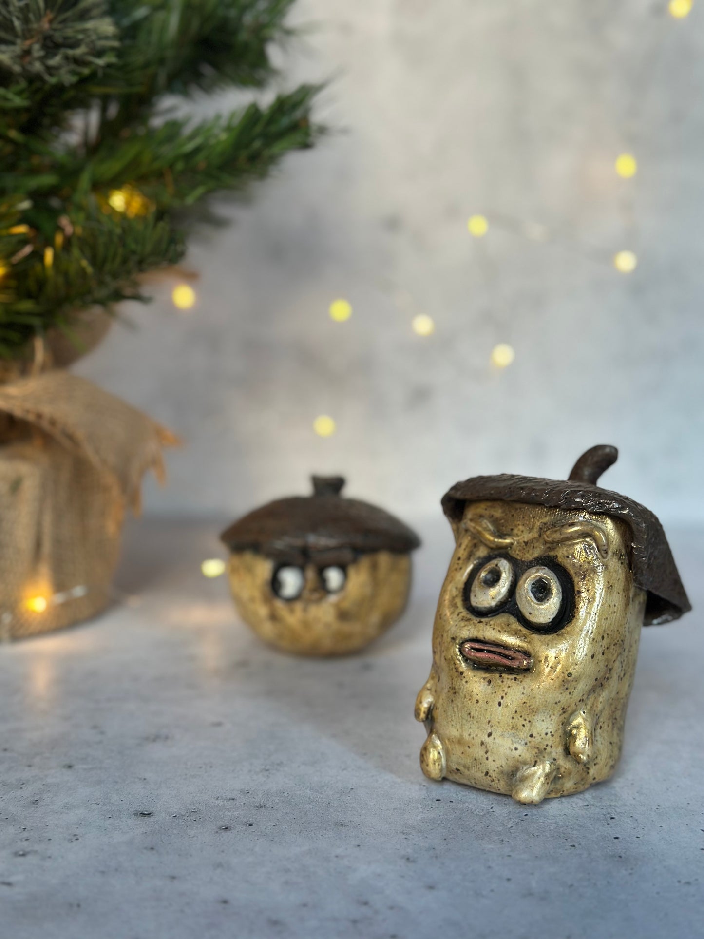 Two small decorative figures resembling acorns with faces on a textured surface with a blurred background.