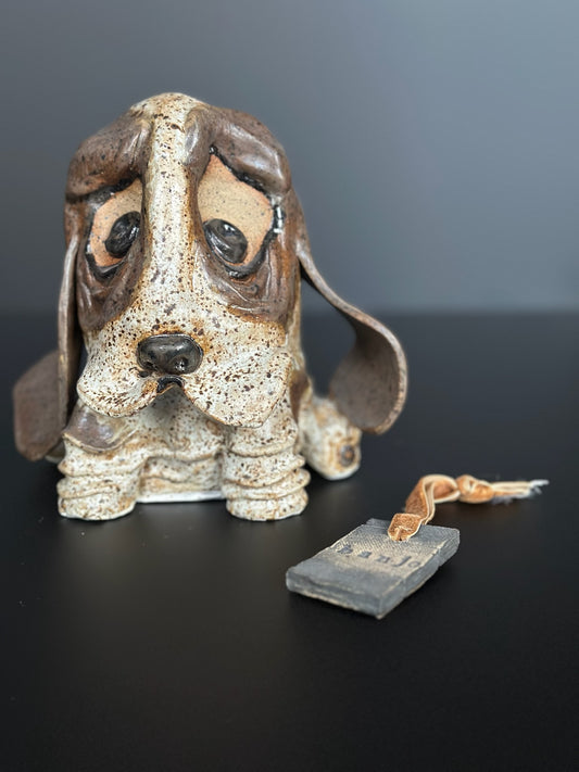 Ceramic basset dog figurine with a tag on a dark surface