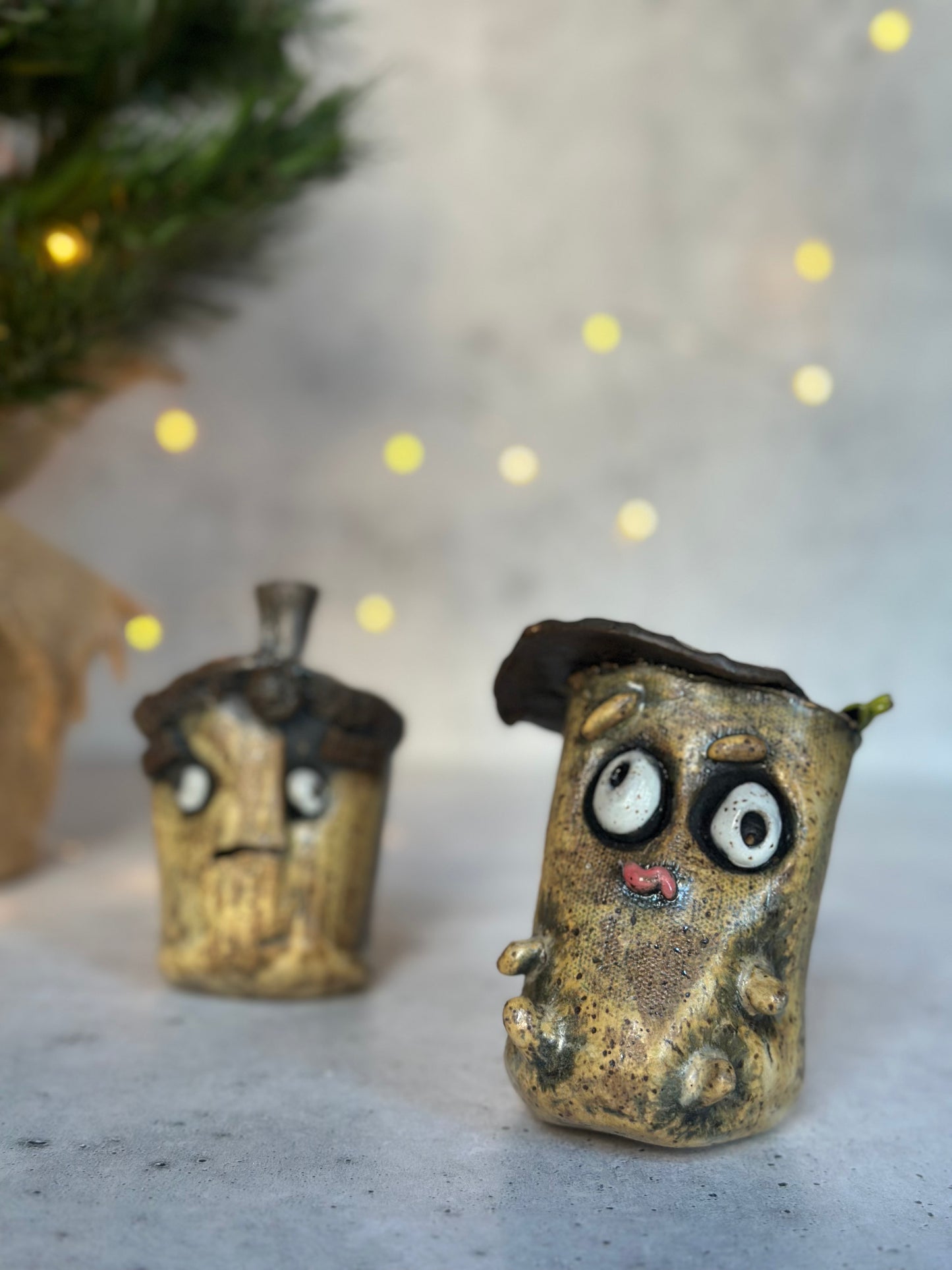 Two small decorative acorns with expressive faces on a neutral background with blurred lights.