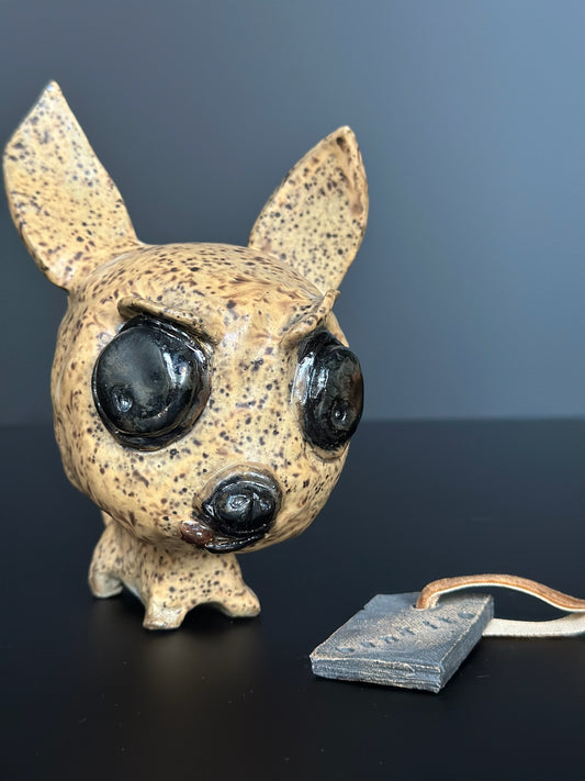 Speckled ceramic chihuahua with black eyes on a dark surface