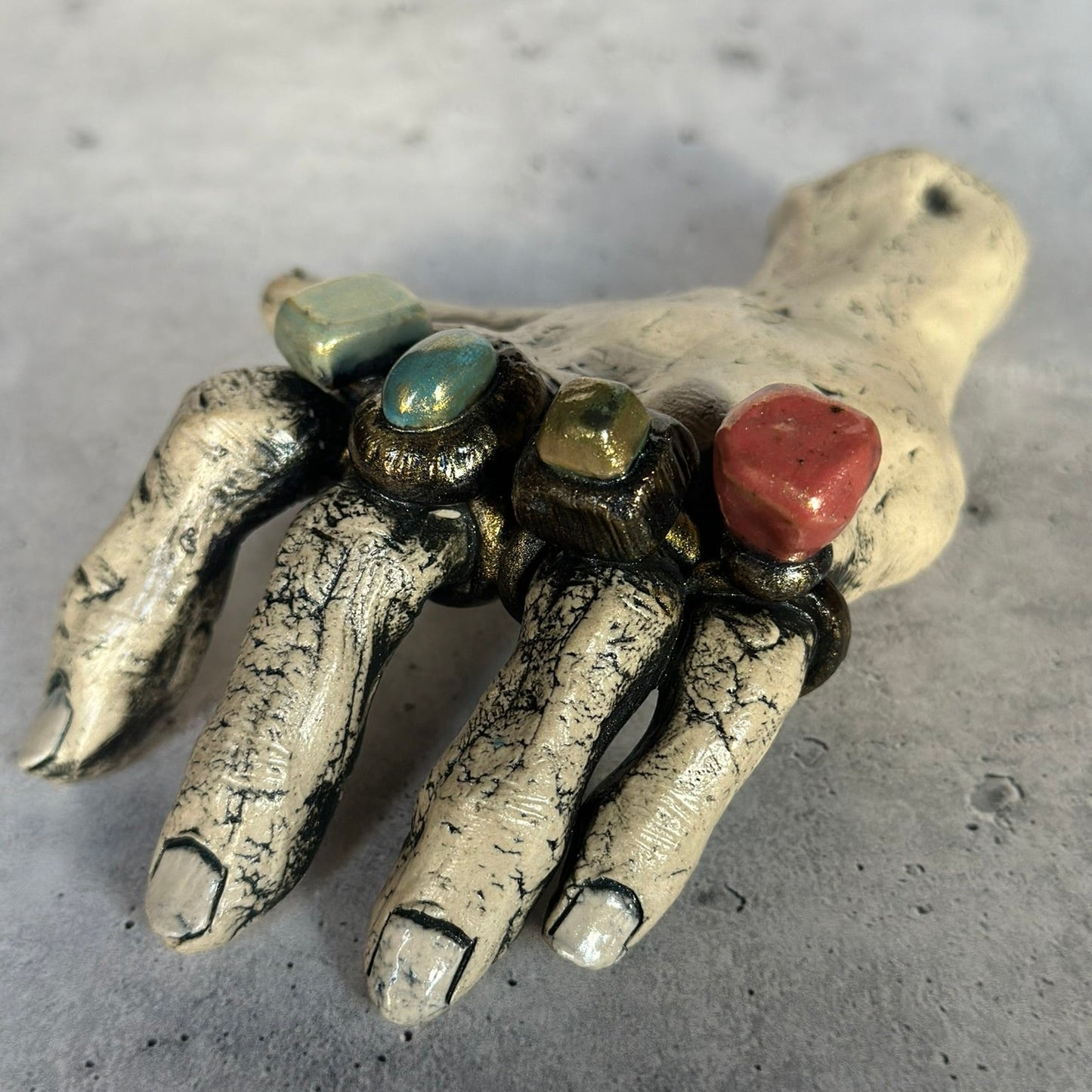 Decorative hand with gemstone rings on a gray surface