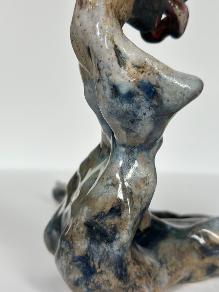 Close-up of a glossy abstract figurative sculpture in mottled gray, blue, and brown tones against a plain light background.