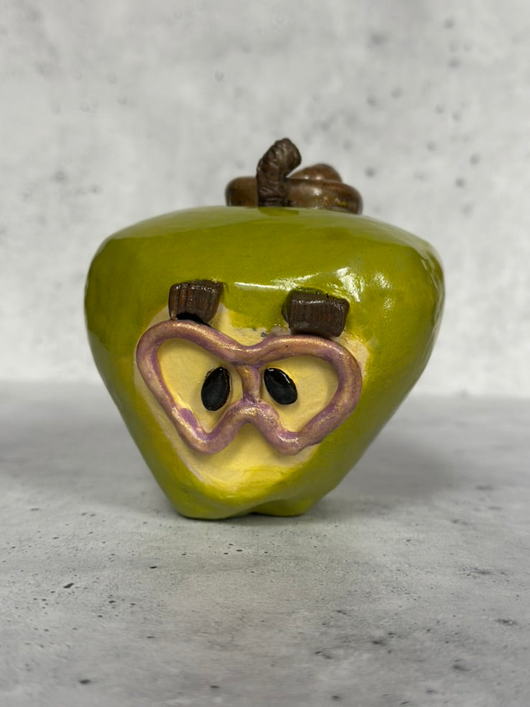 Green ceramic apple with a face on a gray surface