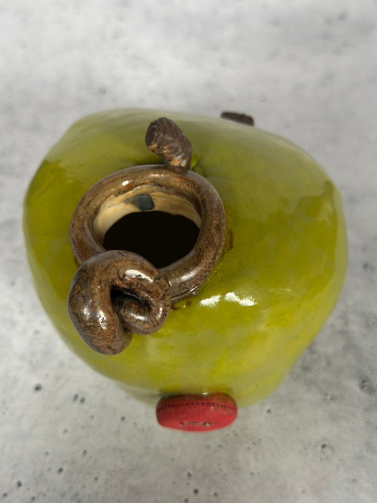 Decorative object resembling a green apple with a bronze knot and red accent on a gray surface