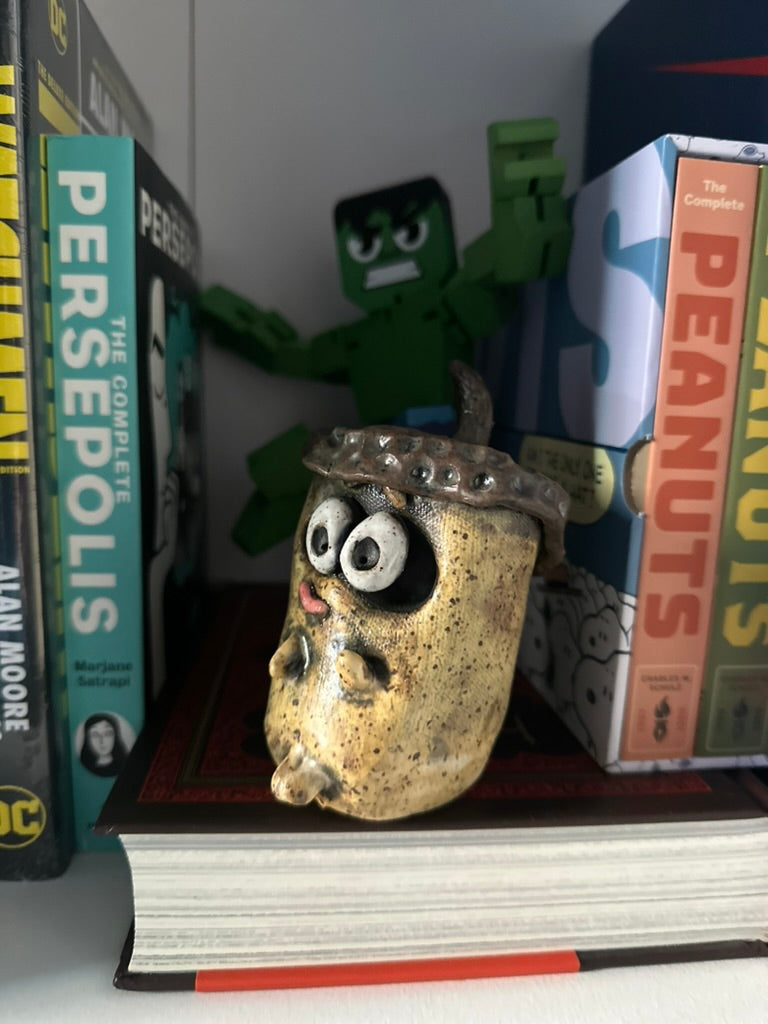 Decorative acorn on bookshelf with a toy figure and comic books in the background