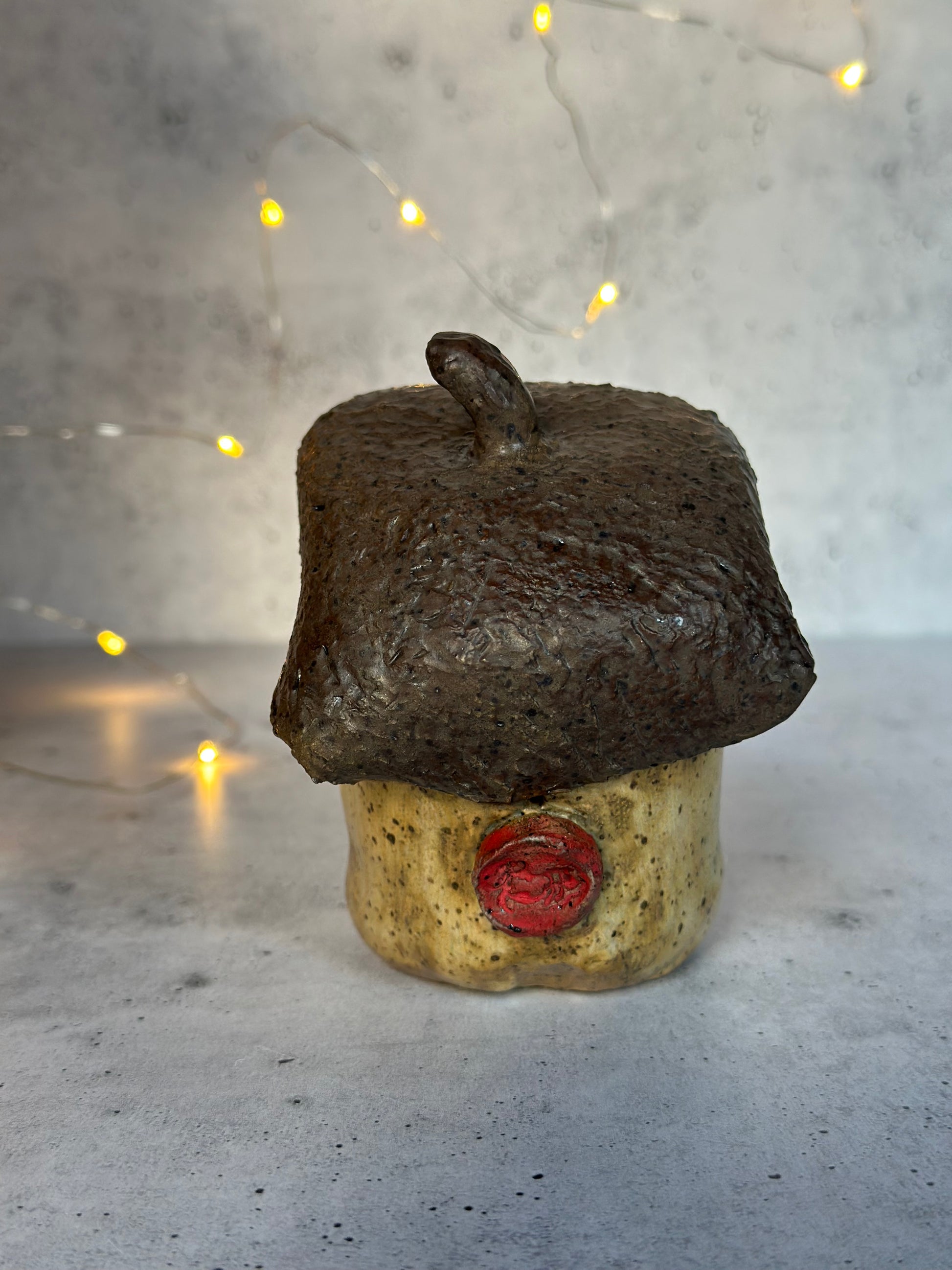 Metallic acorn figure with a face and large eyes on a textured surface back profile