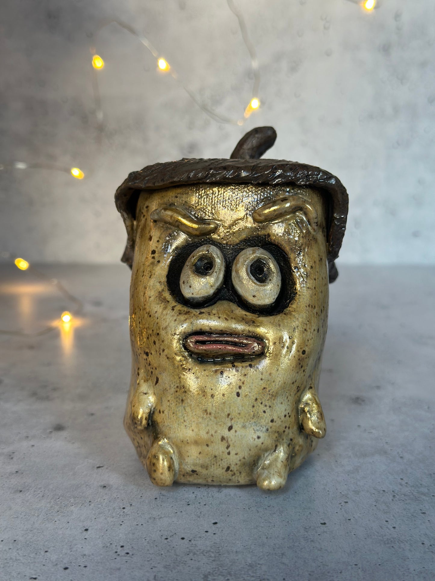 Metallic acorn figure with a face and large eyes on a textured surface