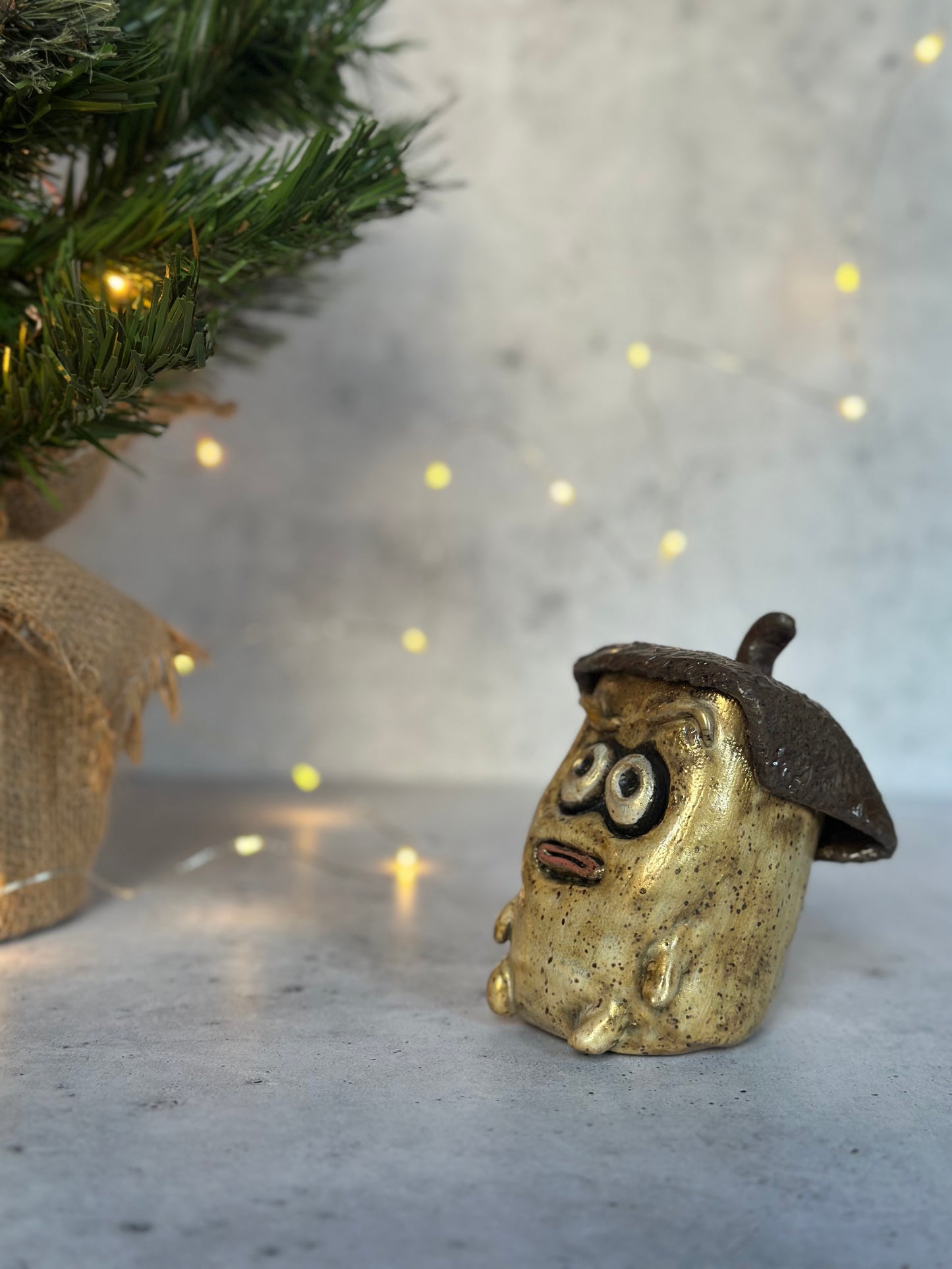 Decorative figurine resembling a creature with an acorn hat on a surface with a blurred background of lights and greenery.