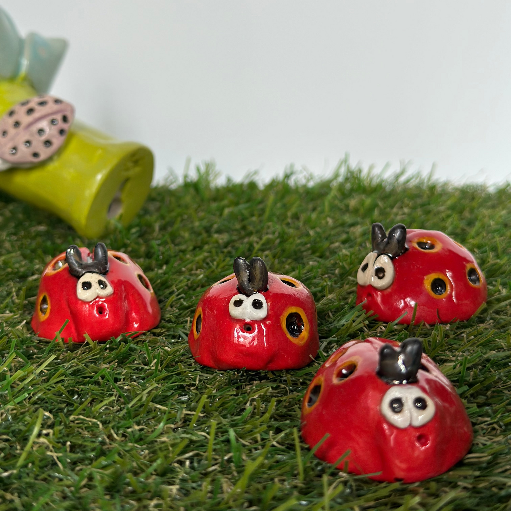 Four red ladybug figurines on grass with a blurred green object in the background