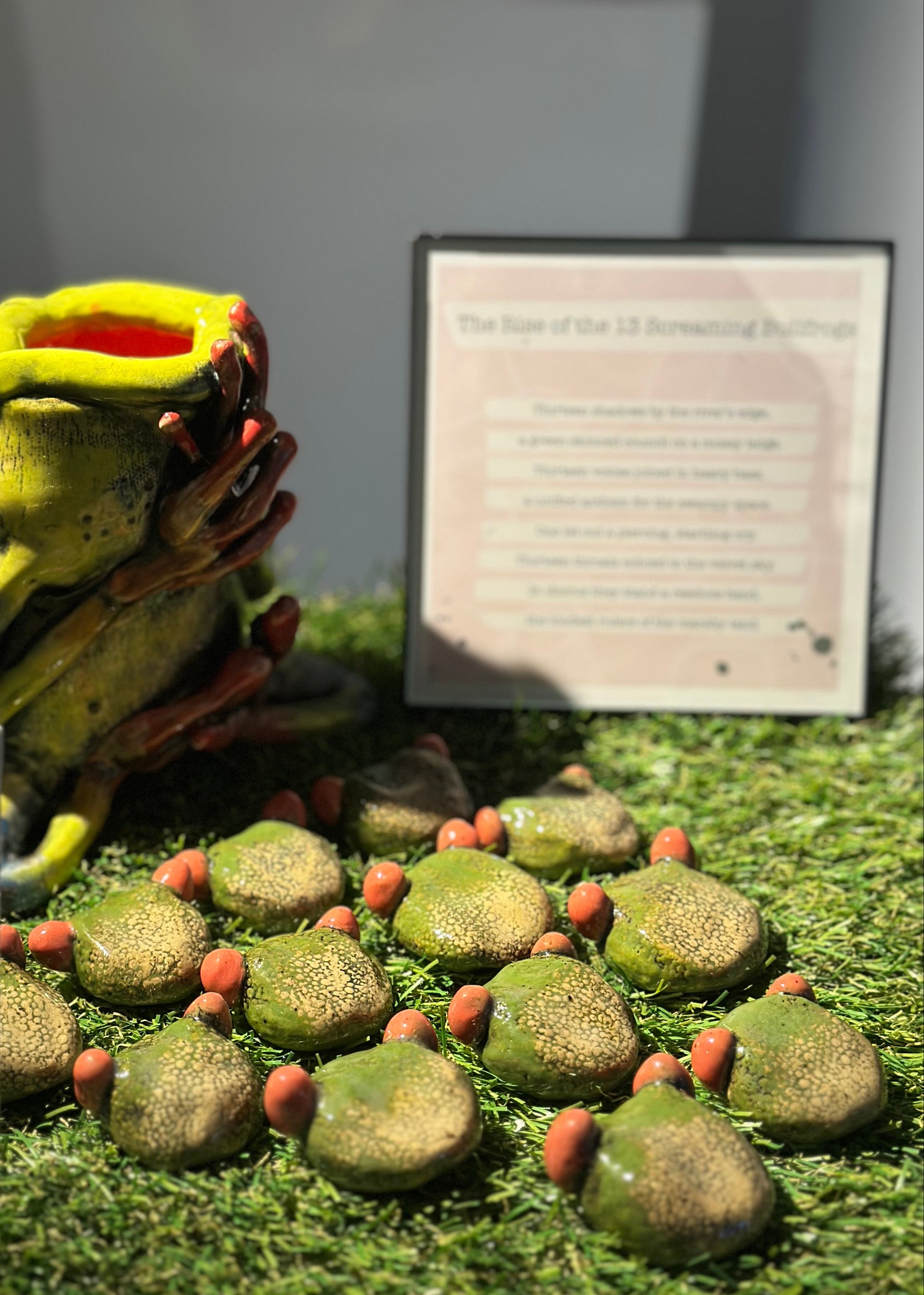 Display of a green frog-like creature with eggs on a grassy surface, accompanied by a sign.