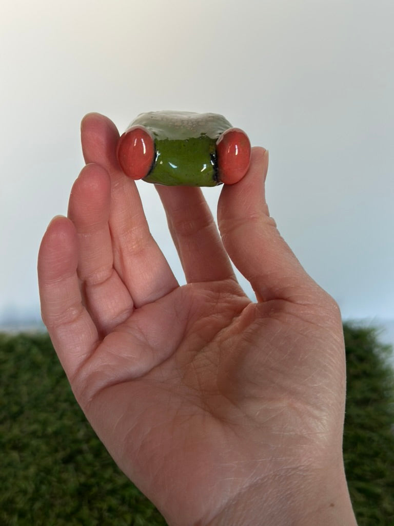 Hand holding a small green frog with a white center against a plain background