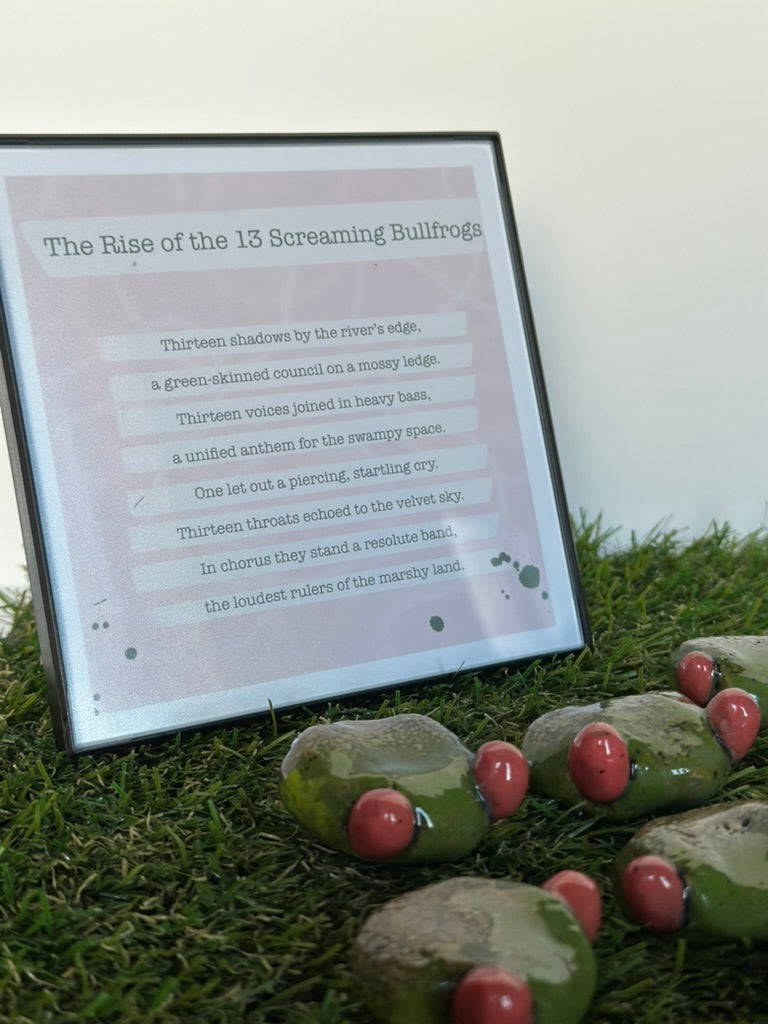 Decorative stones shaped like frogs with red eyes on grass, next to a framed poem.