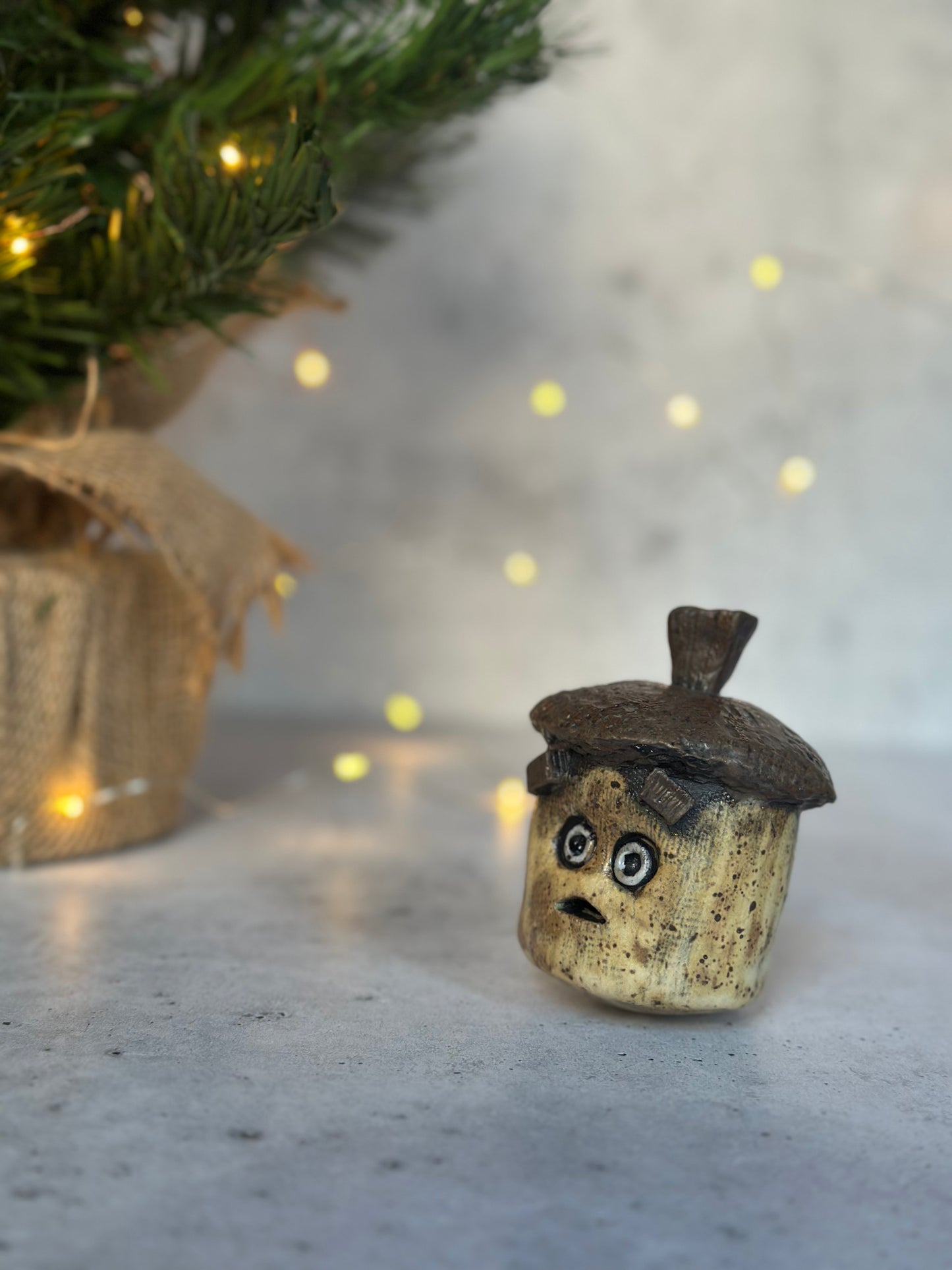 Small acorn with a face on a surface with a blurred background of lights and greenery.
