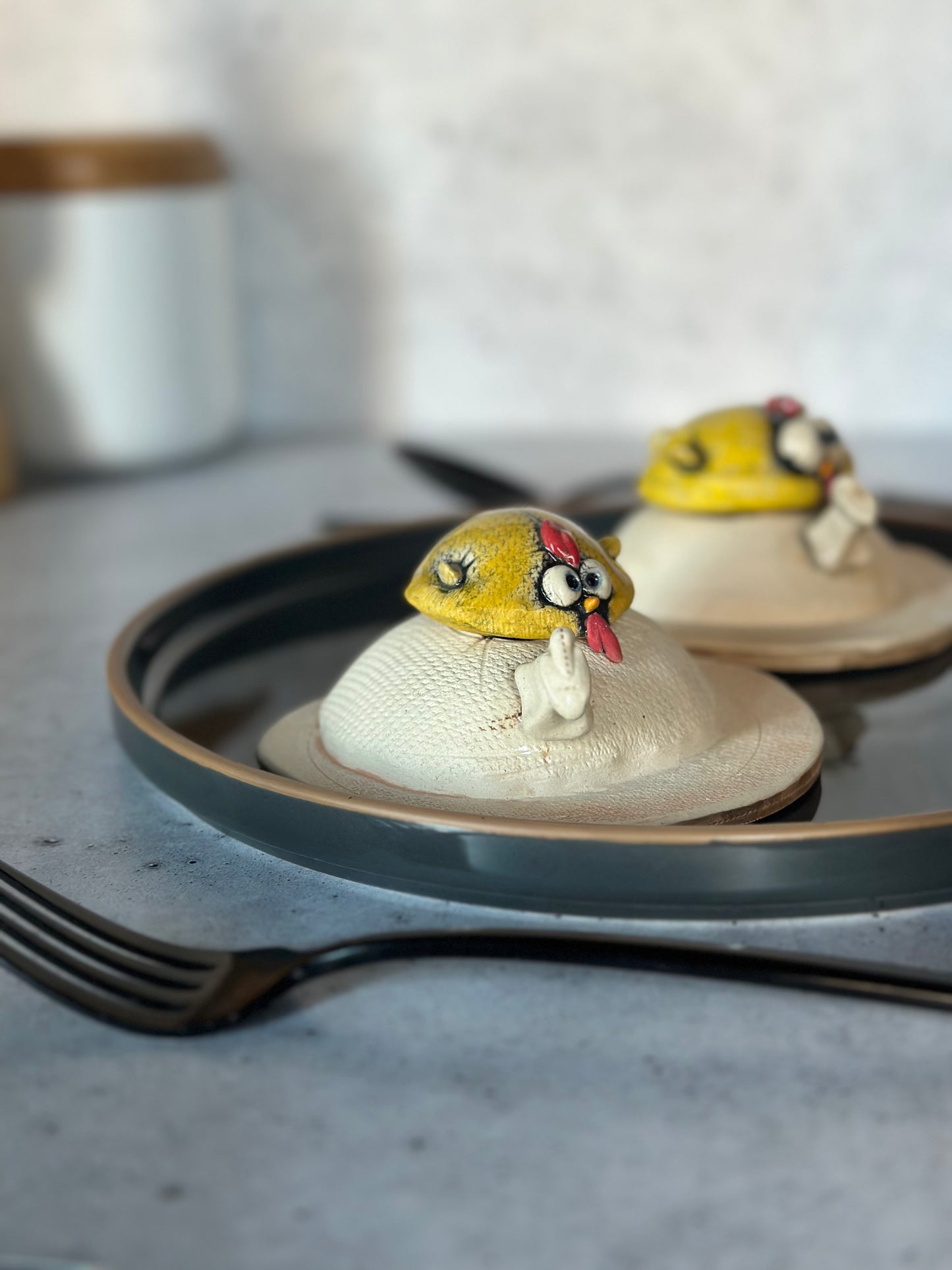 Two small figurines of birds on an egg on a dark plate with a blurred background.