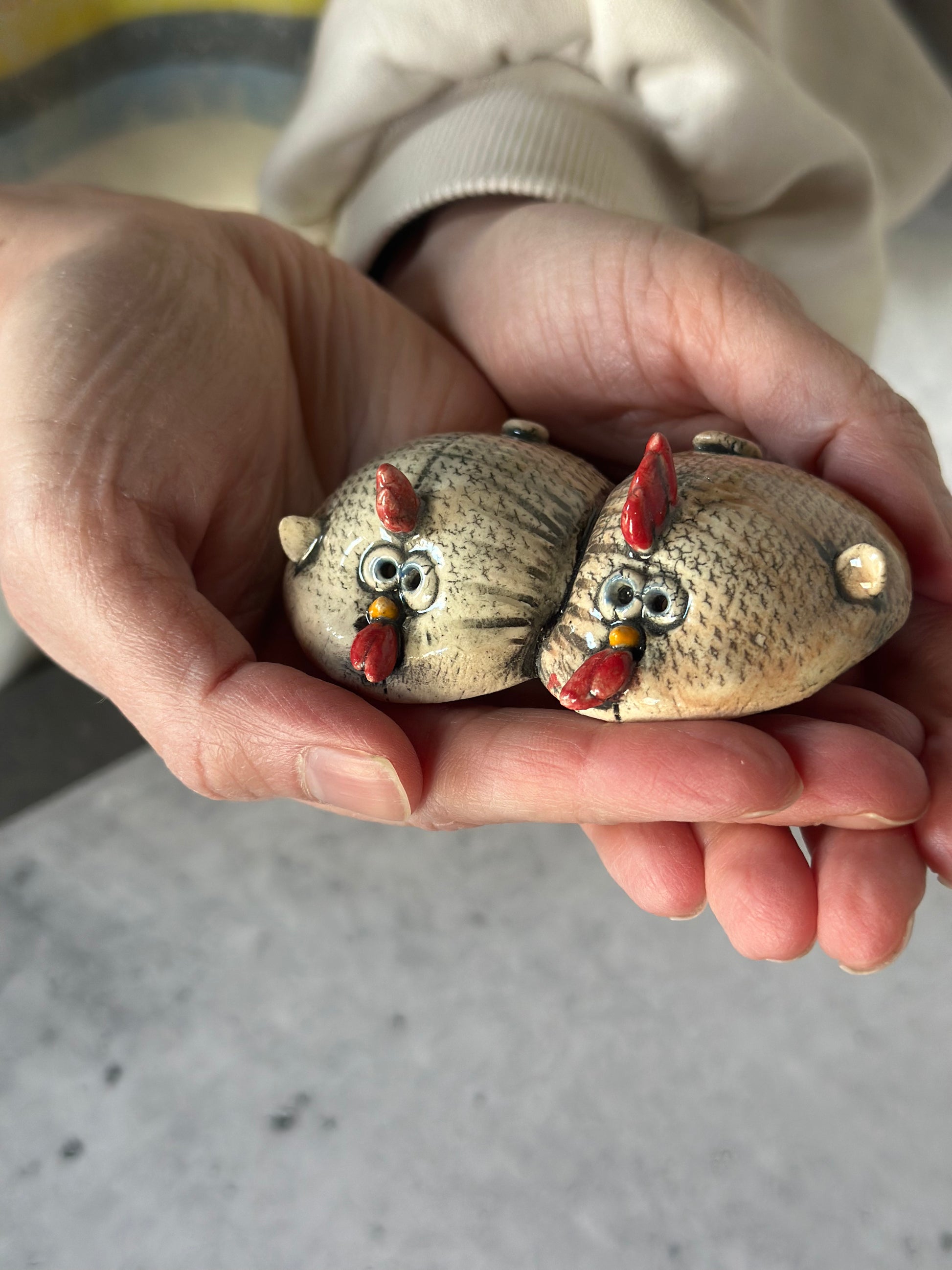 Two painted chickens held in a hand against a neutral background