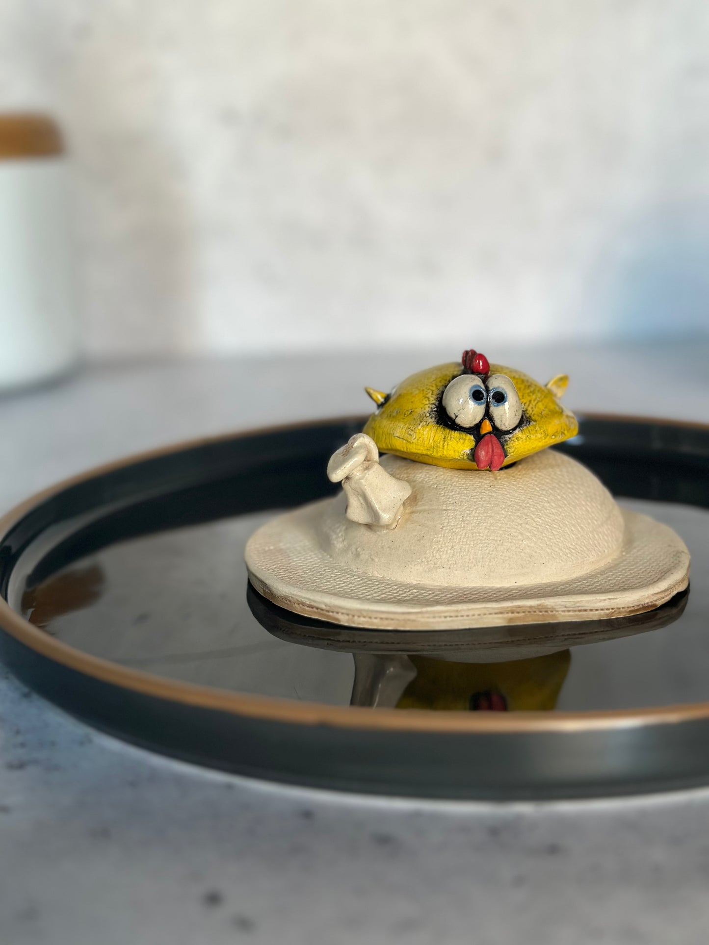 Small ceramic chick figurine on a decorative plate with a blurred background