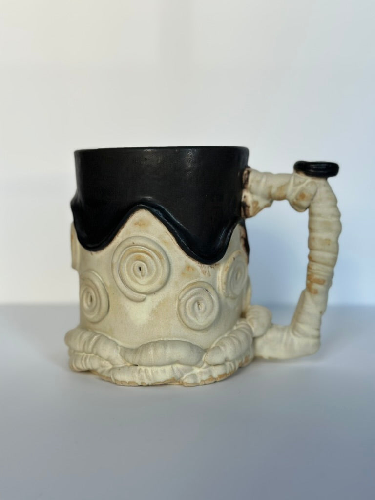Ceramic mug designed like a sheep with a black mouth and white body on a light background