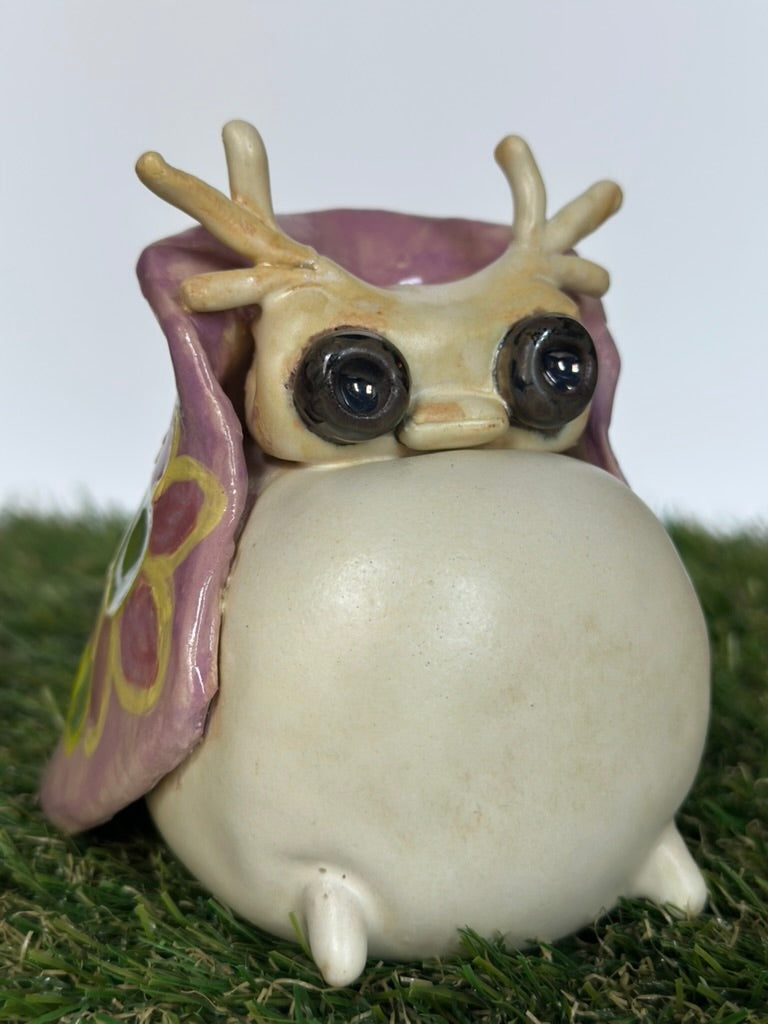 Small ceramic tutrix figurine with a purple flower on a grass-like surface