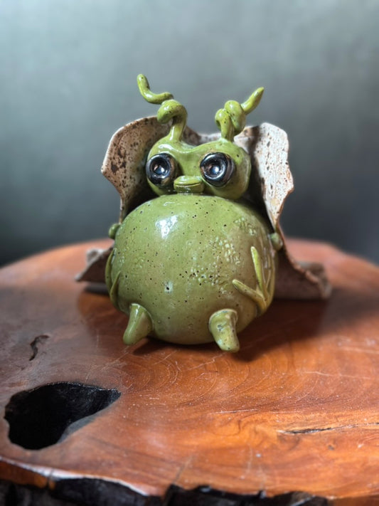 Green ceramic creature figurine on a wooden surface with a dark background