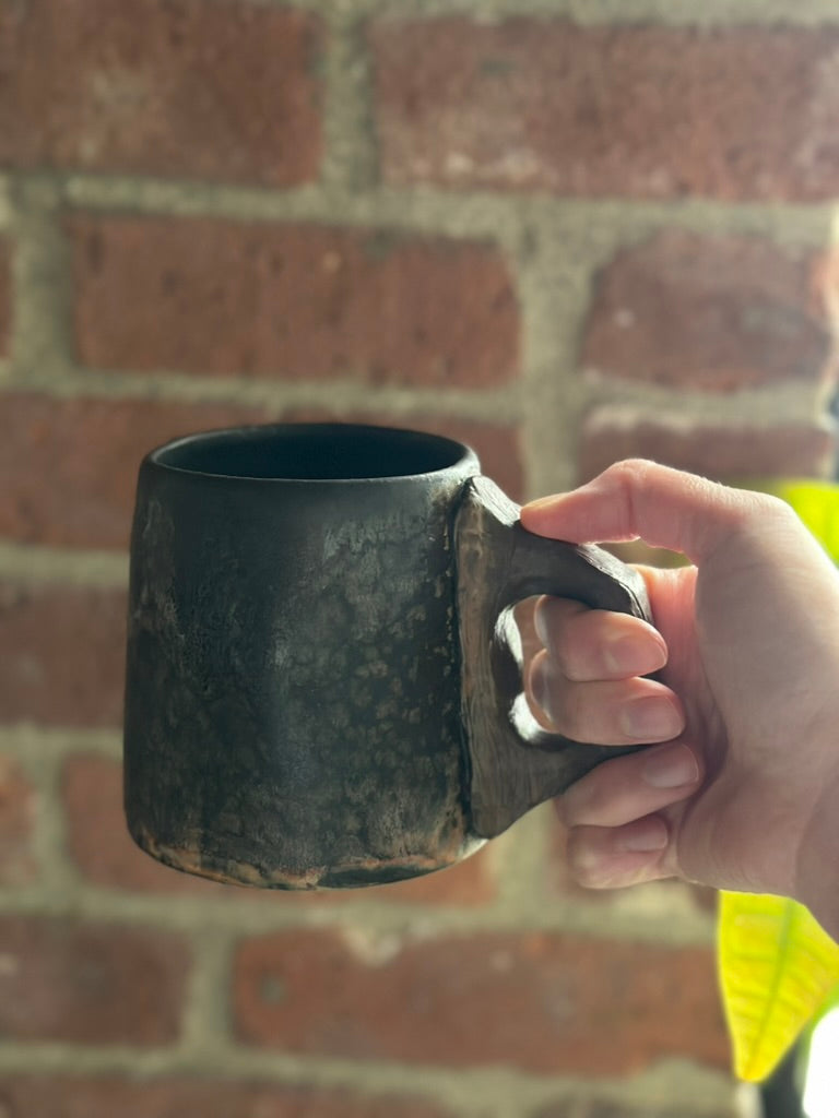 Hand holding a black mug against a brick wall