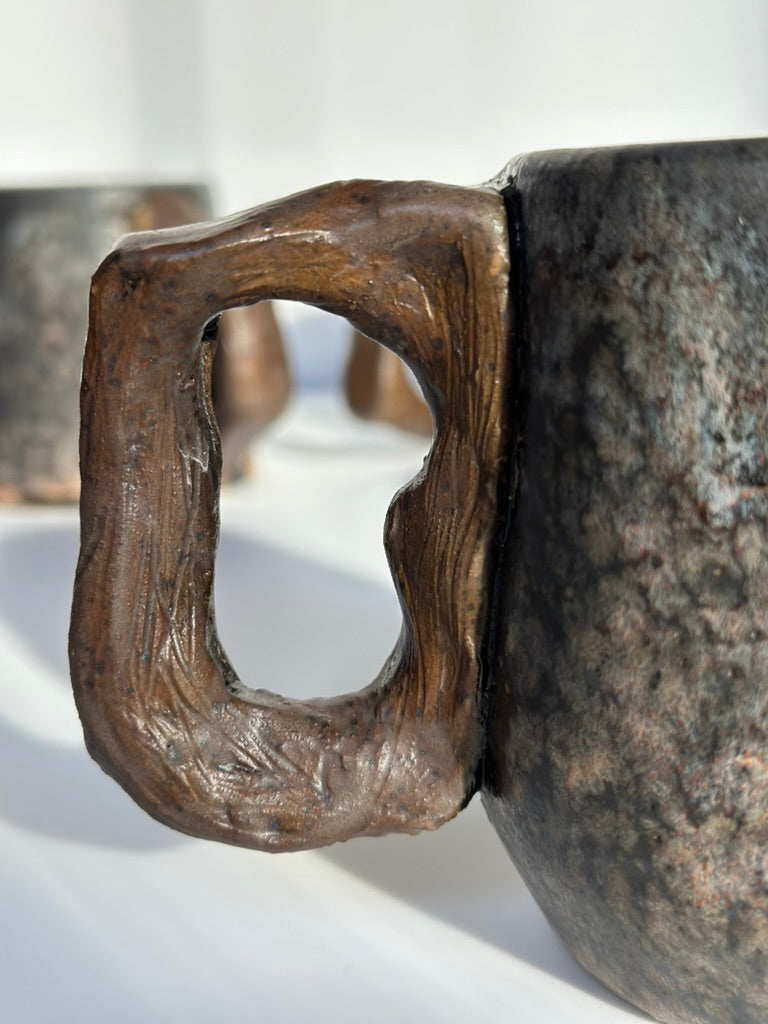 Close-up of a rustic ceramic mug with a wooden handle on a white background