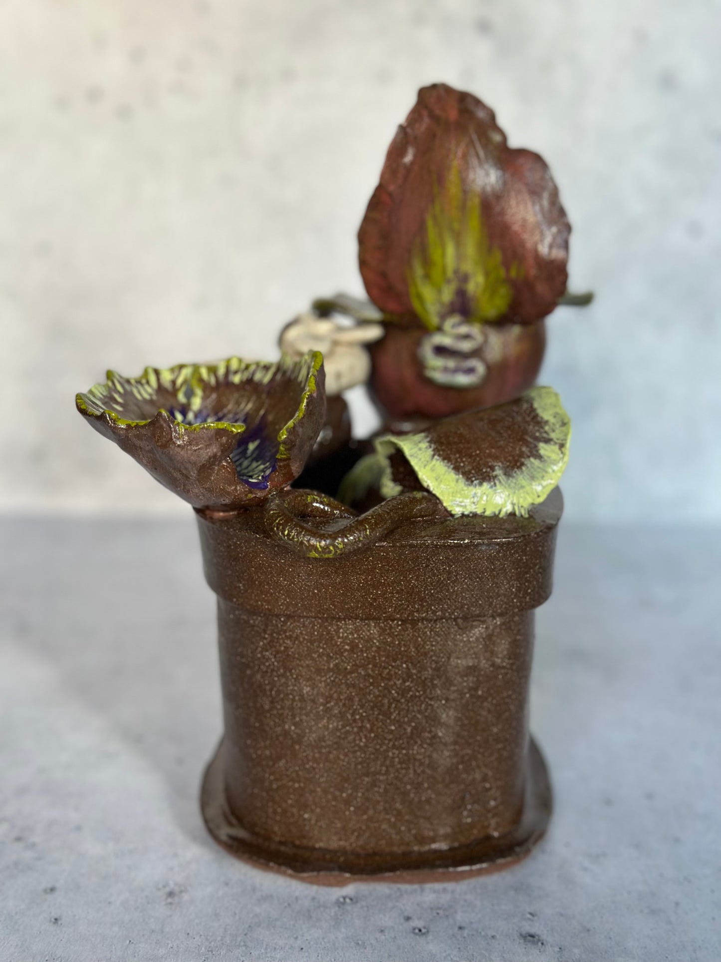 Decorative ceramic piece resembling a flower pot with a plant on a gray surface